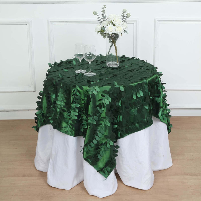 Green leaf tablecloth on a white table with glasses and a floral centerpiece.