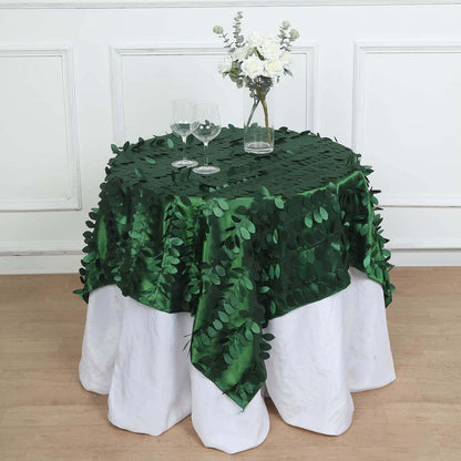 Green leaf tablecloth on a white table with glasses and a floral centerpiece.