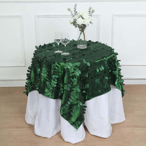 Green leaf tablecloth on a white table with glasses and a floral centerpiece.