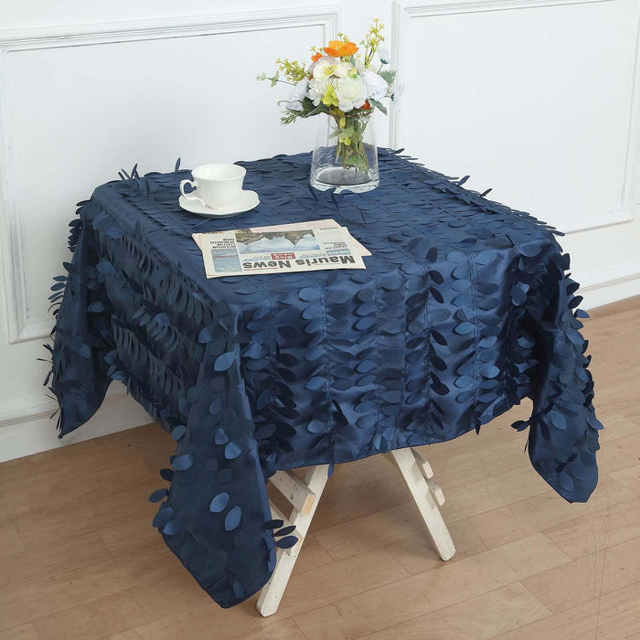Navy blue tablecloth with leaf embellishments on a wooden table with a vase and cup.